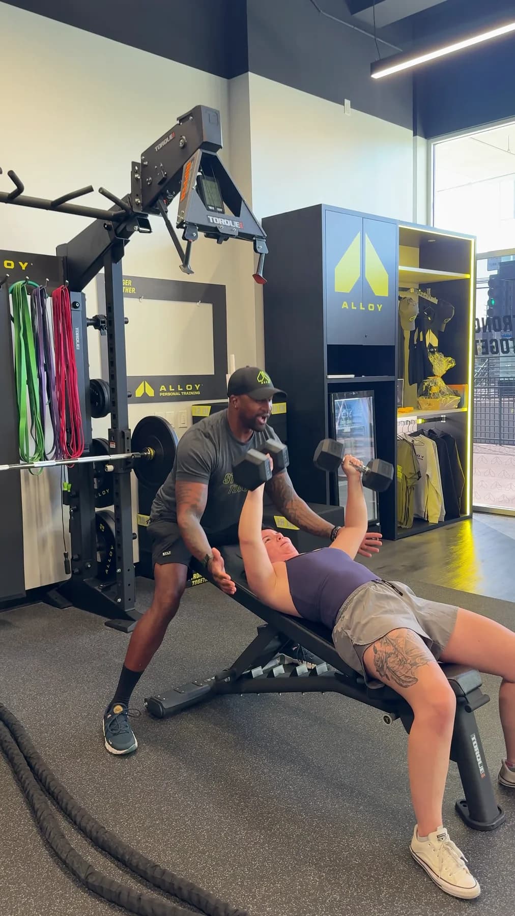 A coach guiding a member through an incline dumbbell press